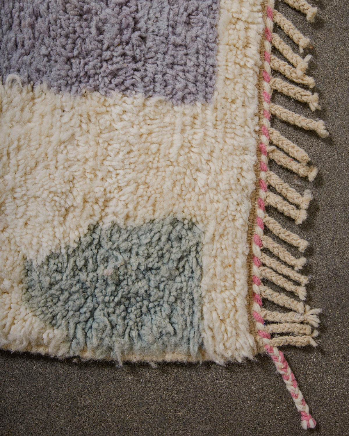 Edge of wool rug with natural cream tassels and details in pink and white.